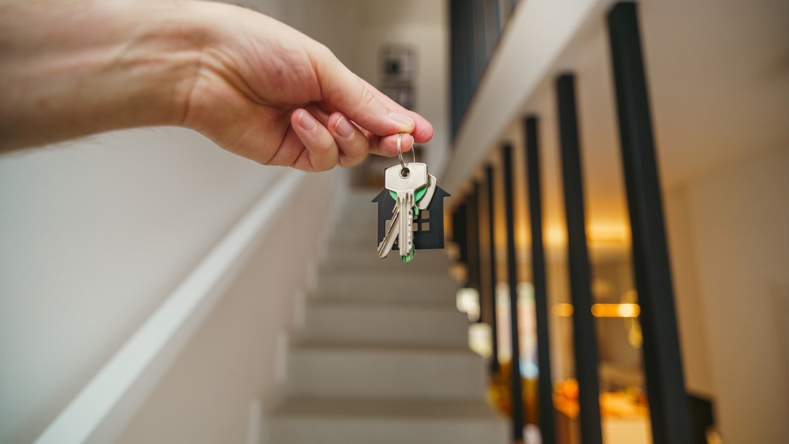 Una mano sostiene unas llaves con un llavero en forma de casa sobre una escalera