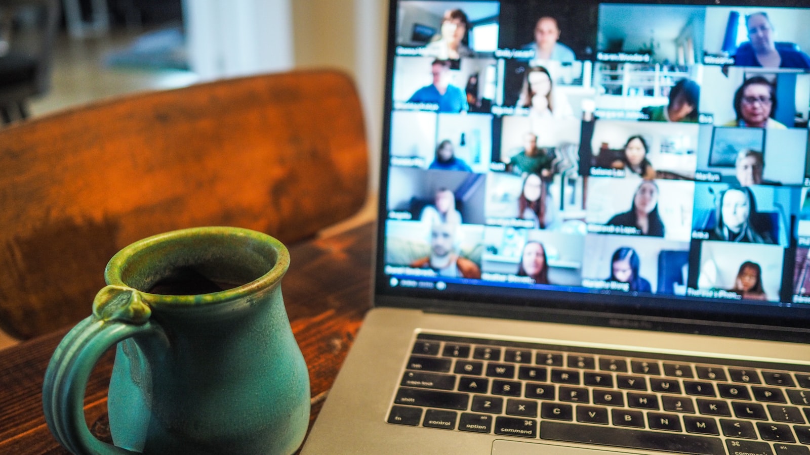 Un portátil con una videollamada en cuadrícula junto a una taza de cerámica verde